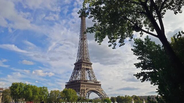 A scenic view of the Eiffel Tower framed by green tree leaves under a cloudy sky in the French capital