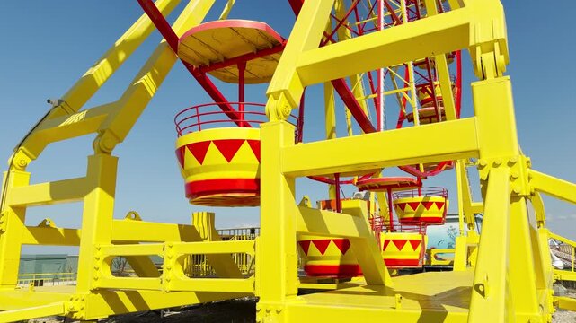 A massive yellow steel frame supports bright red and yellow Ferris wheel cabins on a sunny day. This cheerful scene sparks feelings of eager anticipation, joy, and summer fun.