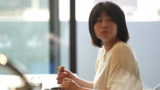 Soft light frames a quiet moment. Woman sips tea, gazes softly beyond the glass. Calm, thoughtful pause in a bright cafe. Perfect for serene lifestyle or quiet moments
