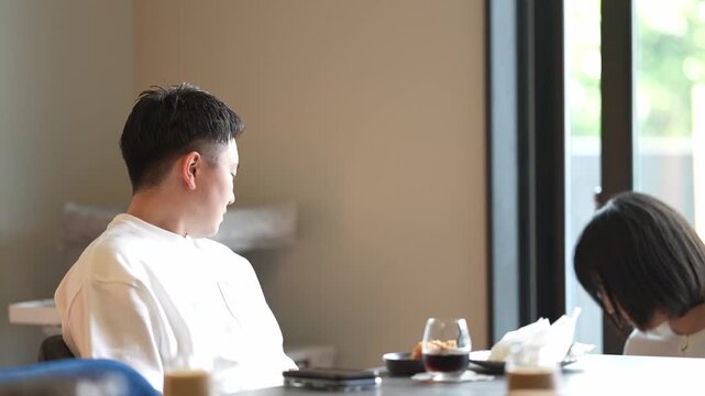 Two people sit quietly at a cafe table. One raises a hand, eyes closed, as if relaxing. Soft light fills the space, calm and peaceful. Perfect for scenes of quiet reflection or casual conversation