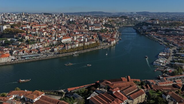 Aerial view of the Douro River flowing through the historic city of Porto, featuring terracotta rooftops, the iconic Dom Luis I Bridge, and boats on the water in Porto, Porto District, Portugal.