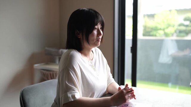 Soft light fills a quiet room. Woman sits, focused on her phone. Her hands move gently over the screen. She looks thoughtful, relaxed, and calm. Good for scenes of modern, peaceful, everyday life