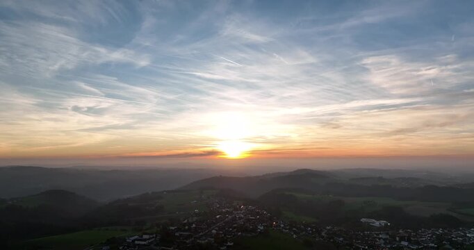 Stimmungsvoller Sonnenuntergang &uuml;ber einer h&uuml;geligen Landschaft mit weitem Ausblick in Niederbayern, warmem Licht, Wolkenhimmel und ruhiger Naturatmosph&auml;re.
