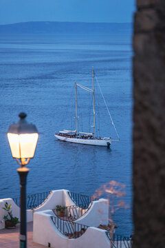 Luxury two-masted yacht anchored in the blue sea at dusk behind a blurry streetlight
