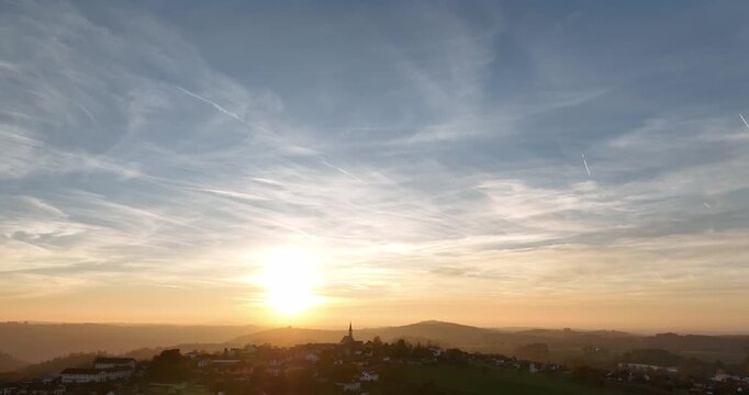 Stimmungsvoller Sonnenuntergang &uuml;ber einer h&uuml;geligen Landschaft mit weitem Ausblick in Niederbayern, warmem Licht, Wolkenhimmel und ruhiger Naturatmosph&auml;re.