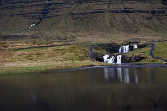 Kirkjufellsfoss waterfall cascading into a calm lake with a mountain backdrop, Iceland