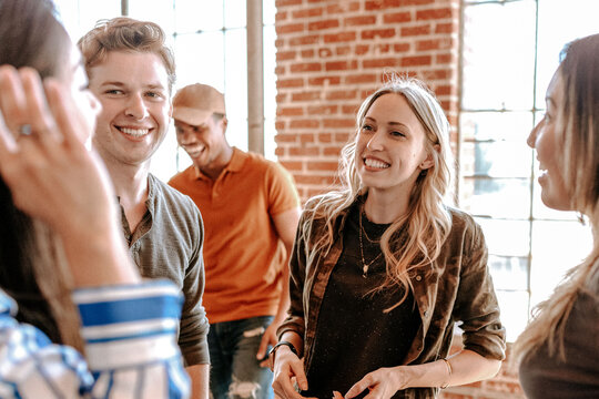 Group of people smiling and chatting in a casual setting with brick walls and windows.
