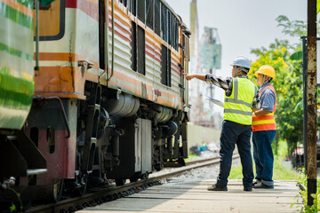 Engineers inspecting a used train car on railway tracks. Professionals in safety gear assess train condition and surrounding construction, highlighting rail maintenance and infrastructure development. © Peemapat