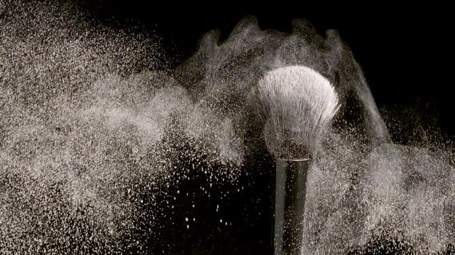 Slow-motion intimate close-up of black brush flicking light beige powder on a plain black background | Promotional concept for powder foundation