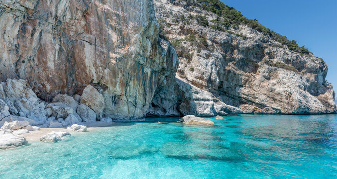 transparent water on little beach below steep rocky cliffs at Cala Mariuolo, Cala Gonone, Italy