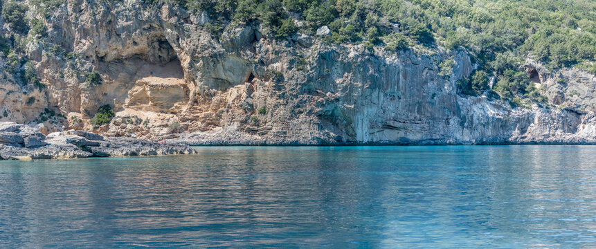 steep rocky shore with cavern hollows on blue transparent water near Fico cavern, Cala Gonone, Italy