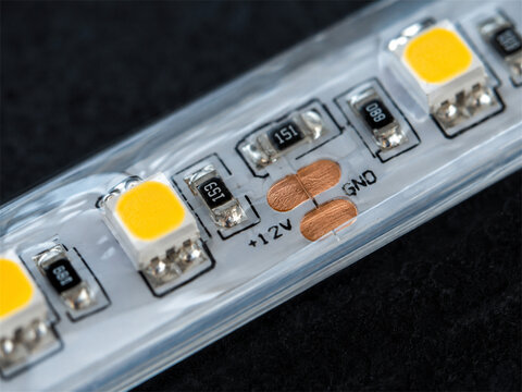 Macro view of flexible led light strip with yellow diodes resistors and copper contacts on clear casing showing electronic circuit detail for lighting repair technology and hardware background