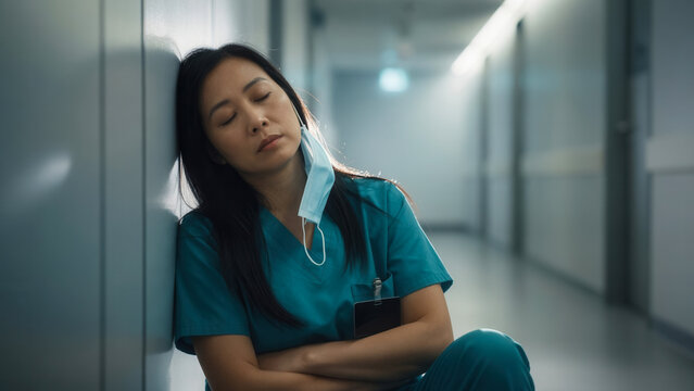 Tired Asian medical professional resting on floor in hospital hallway, health care burnout and overwork in medicine