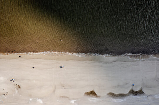 Jekyll Island, Georgia, United States - 31 December 2021: Aerial view of the sandy beach shoreline with gentle waves meeting the coast and people walking along the sand.