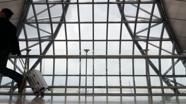 Passenger mixed up the boarding time or confused the gate for boarding and runs to plane through an empty airport. Slow motion shot, dim natural light at modern terminal, glass wall on background