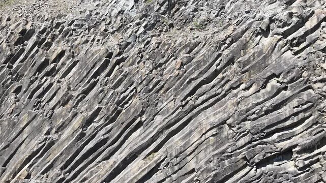 Close-up aerial view of rugged rock formations with a smooth backward movement revealing detailed cliff textures and natural geological patterns.