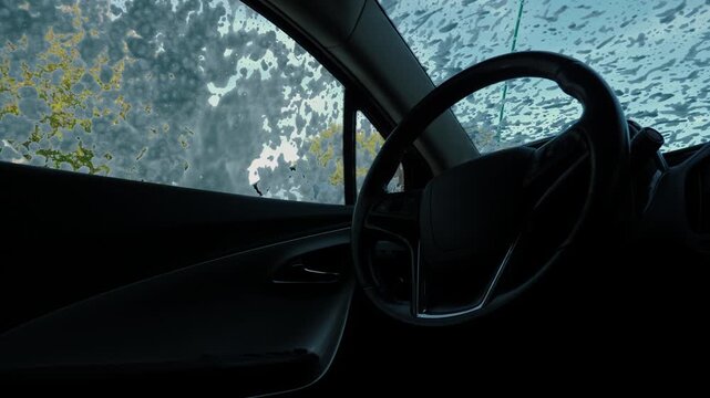 Driver-side cabin seen from inside as foam streaks cover the windshield and side window. Washing a car on the street. Clean the car