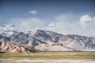 A mountain landscape featuring rocky peaks and snow-capped glaciers, with a valley containing fields, pastures of fresh green grass, and clear-water rivers—suitable for a background image © Denis
