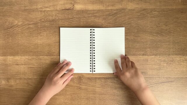 Child Hands Close a Small Ring Notebook on a Wooden Table, 4K