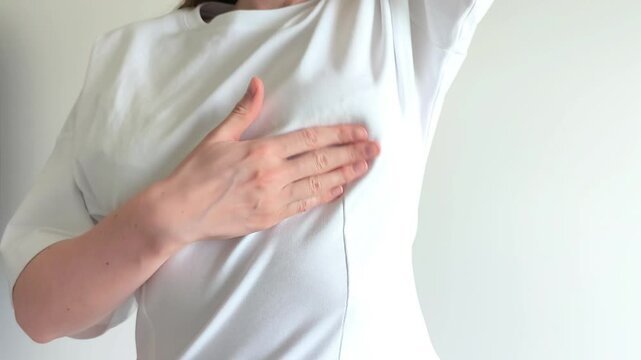 Woman performs a breast self examination feeling for lumps under her shirt. She checks her chest carefully searching for any unusual changes or masses. Concept of breast cancer awareness,