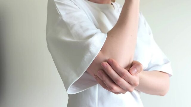 Woman massages her elbow with her hand easing pain from a recent injury. She rubs her arm gently feeling discomfort in the joint. Concept of elbow pain, bruise and joint injury recovery..