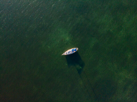 Key Largo, Florida, United States - 24 December 2019: Aerial view of a lone sailboat drifting in clear turquoise waters, casting a long shadow on the sandy seabed below.