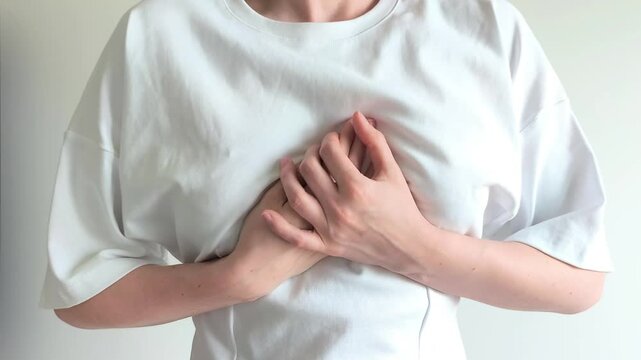 Woman clutches her chest with both hands feeling sudden sharp pain. She presses against her sternum reacting to discomfort in her upper body. Concept of chest pain, heartache and solar