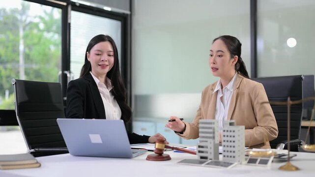 Two professional Asian businesswomen review corporate financial reports and real estate investment data in a modern office.