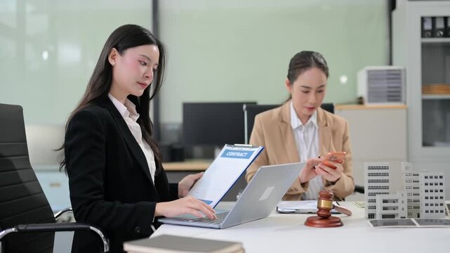 Two professional Asian businesswomen review corporate financial reports and real estate investment data in a modern office.