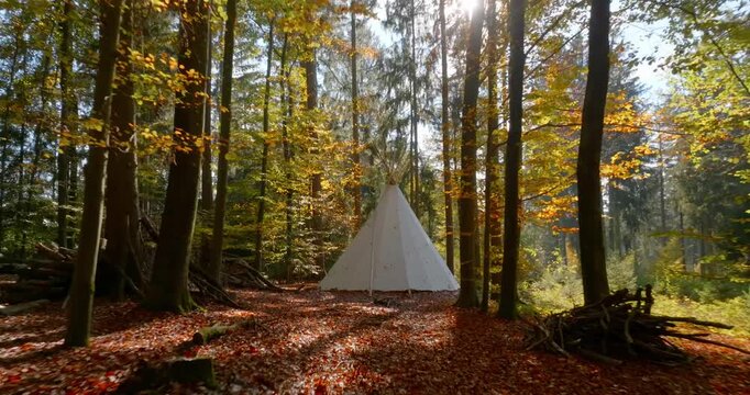 Wei&szlig;es Tipi-Zelt in einem herbstlichen Wald, umgeben von B&auml;umen, Laub und warmer Naturstimmung, als ruhige Outdoor-Szene f&uuml;r Camping, R&uuml;ckzug und Erholung