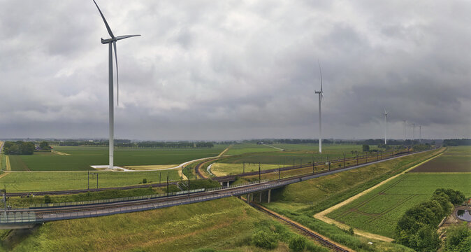 Moerdijk, North Brabant, Netherlands - 27 May 2025: Aerial view of the Moerdijk railway line with Vattenfall wind turbines, set against green agricultural fields under a cloudy sky.