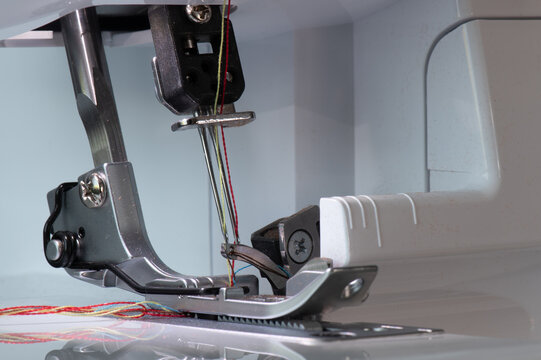 Overlock sewing machine with lowered foot, needle at the top, and carrier with close-up view from diagonally left