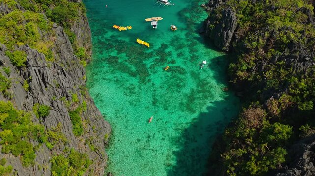 Aerial Forward Tracking Shot Over Small Lagoon in El Nido, Philippines. Drone View with 45-Degree Downward Angle of Turquoise Water, Limestone Cliffs, and Kayaks.