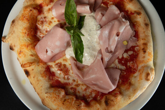 Une pizza avec du jambon et du basilic au restaurant &agrave; midi