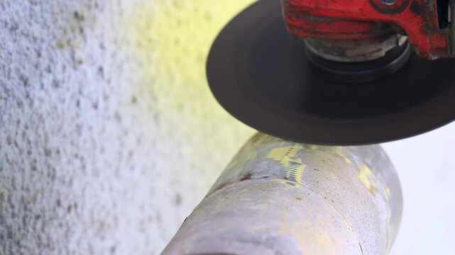 Close up of an angle grinder stripping old paint from a metal pipe surface