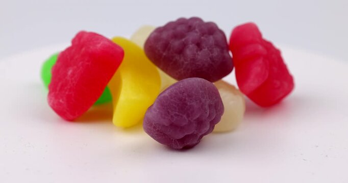 Horizontal view of assorted fruit shaped gummies turning on a rotating plate device zone arranged on a plain table workspace desk