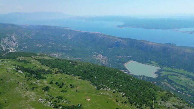Breathtaking aerial view of the lush green hills meeting the serene blue Adriatic Sea in the Kvarner Gulf, Croatia. Scattered villages dot the picturesque coastline. Tribaljsko jezero