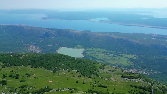 Breathtaking aerial view of the lush green hills meeting the serene blue Adriatic Sea in the Kvarner Gulf, Croatia. Scattered villages dot the picturesque coastline. Tribaljsko jezero