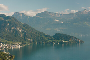 Fototapeta premium Aerial view of a wooded peninsula on a Swiss alpine lake with layered mountains fading into atmospheric haze on a summer day