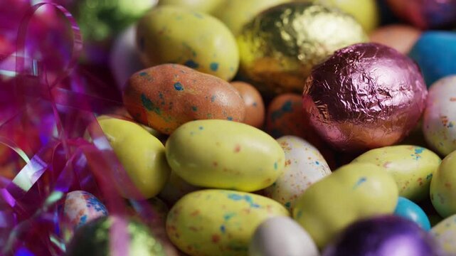 Assorted colorful foil wrapped chocolate Easter eggs and speckled candies with decorative ribbons in a close up shot