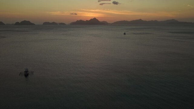 Aerial Backwards Reveal and Descent over Corong Corong Beach at Sunset in El Nido, Philippines. Drone View Pulling Away and Dropping Low over Ocean by Mountain Silhouettes.