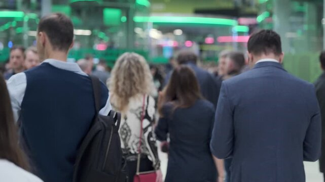 Business commuters waiting in crowded indoor queue, blurred backs of people, urban commute atmosphere, fluorescent lights, weekday rush.