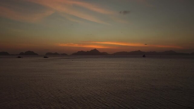 Aerial Descent Over the Ocean at Sunset on Corong Corong Beach in El Nido, Philippines. Cinematic Drone Vertical Pedestal Down View of Golden Dusk Sky and Calm Sea.