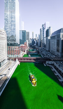 Chicago, United States - 17 March 2019: Aerial view of the Chicago River dyed green for St. Patrick's Day, with a boat navigating between historic bridges and skyscrapers.