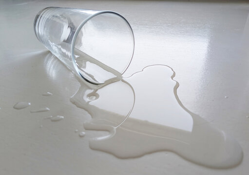 Umgekipptes Glas mit versch&uuml;ttetem Wasser auf hellem Tisch