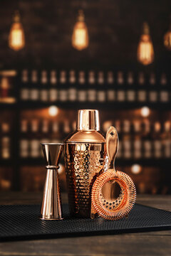 Shaker, jigger, strainer and mixing glass are on bar counter. Glossy surface. Classic accessories for bartender. Black Bar mat. Copper-colored bar accessories