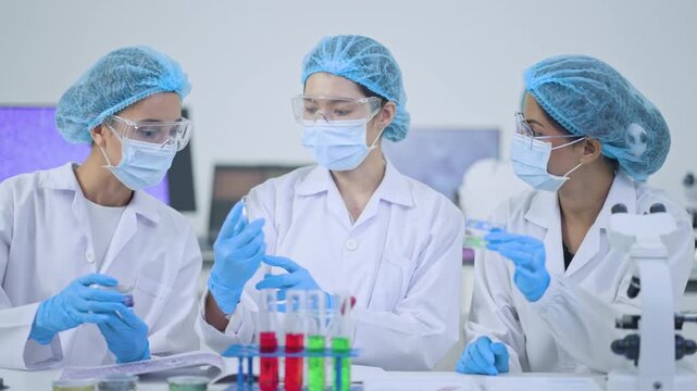 Team of women researchers in masks and hairnets holding specimens at laboratory bench with test tubes and microscope, science teamwork concept.