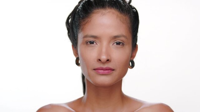 Close-up shot of latin american woman with bronzed skin stretches her cheek skin highlighting elastic skin against white background | Skin care commercial concept