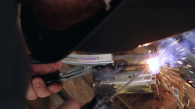 Close up of a welder hand holding ground clamp on a metal pipe with sparks
