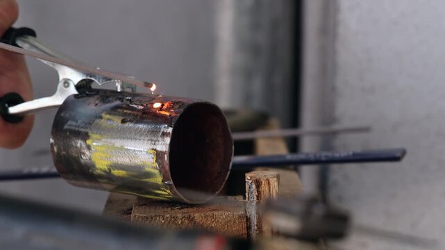 Close up of a metal pipe with welding ground clamp and flying sparks in a workshop